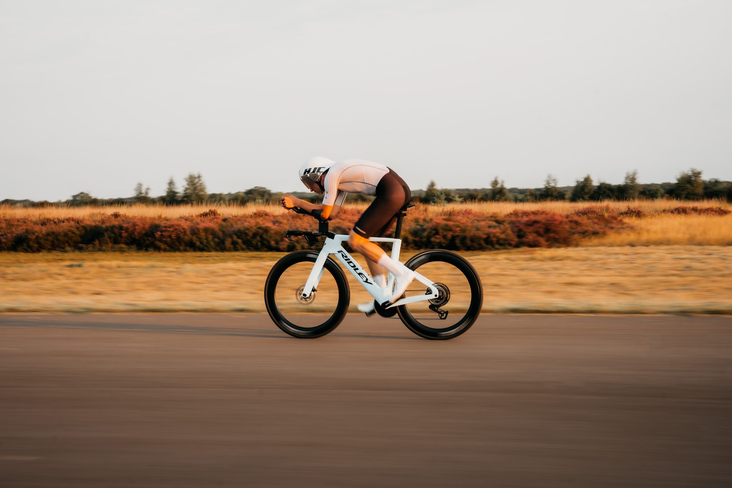 Cyklist i aeroposition på en vit Ridley Triton, sedd från sidan i kvällsljus.